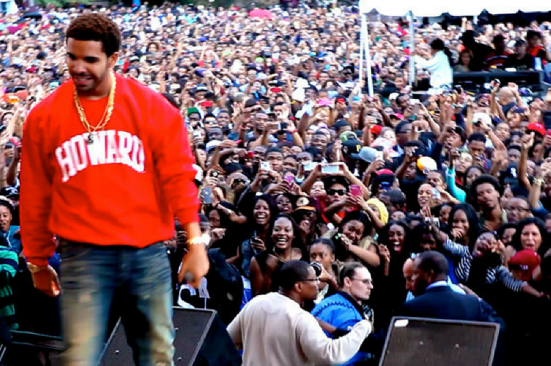 Rap artist 'Drake' is wearing a red sweatshirt standing in front of a crowd